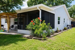 A modern house with a covered patio, a garden with red flowers, and a clear sky. - Your home away from home II (New Port Richey)