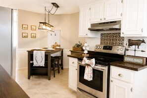A kitchen with white cabinets, a stainless steel oven, a farmhouse sink, and a decorative cow statue. - Your home away from home II (New Port Richey)