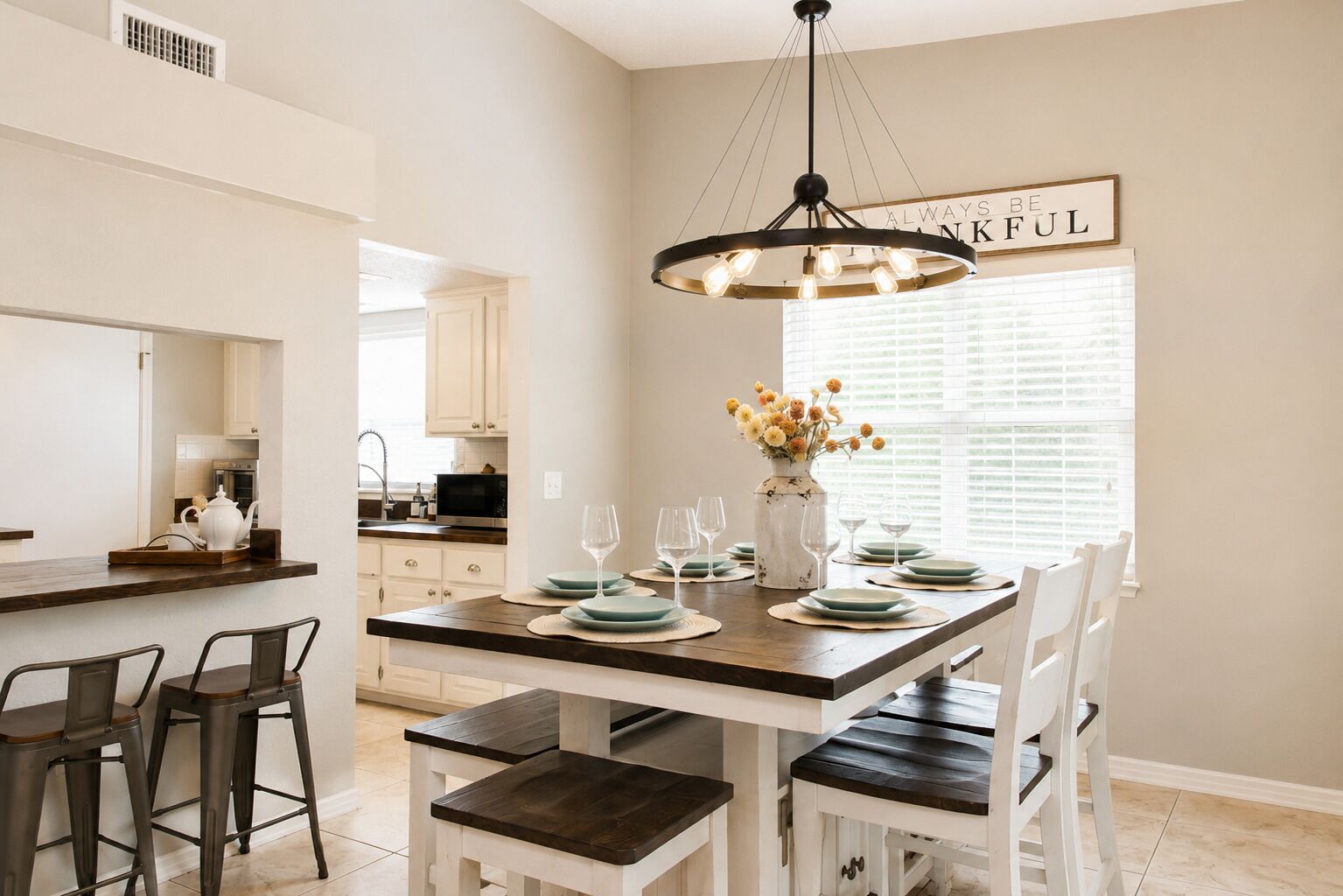 A dining area with a central table set for four, surrounded by white chairs.