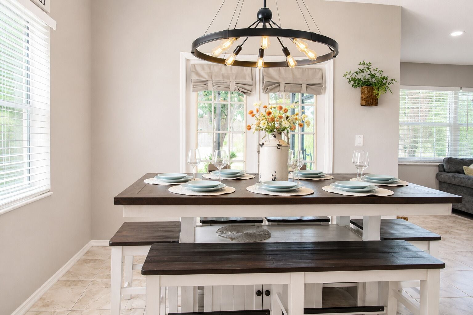 Un comedor con una mesa de madera preparada para cuatro personas, una lámpara colgante y un jarrón con flores.