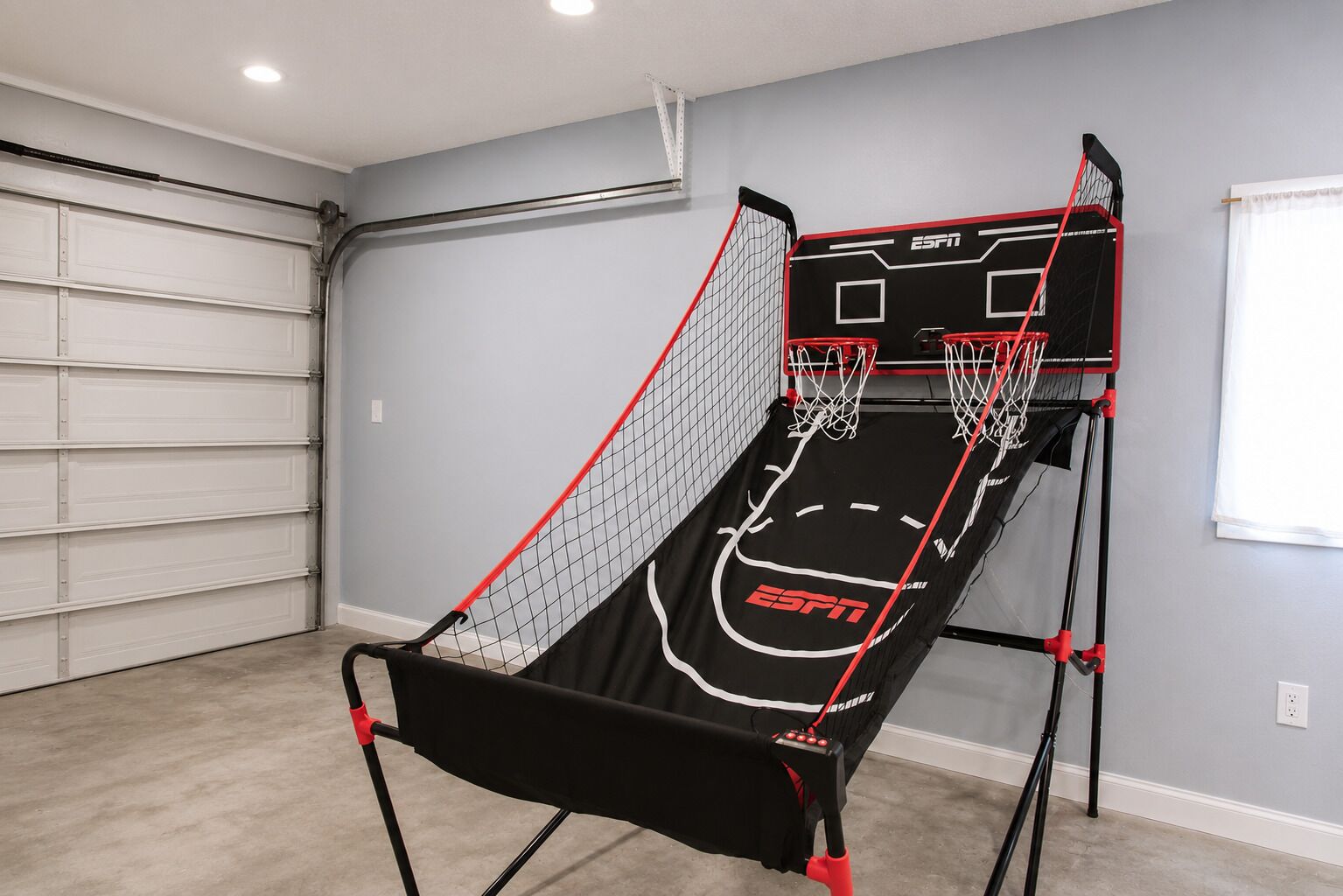 Un panier de basket avec un filet, fixé sur un support, dans une pièce dotée d’une porte de garage et d’une fenêtre.