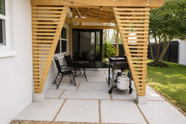 A covered patio area with a table and chairs, a grill, and a propane tank. - Your home away from home II (New Port Richey)
