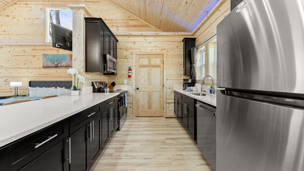 A modern kitchen with wooden walls, stainless steel appliances, and a central island. - True Love Cabin — A Romantic Escape Above the Pines (Cleveland)