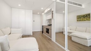 Uma sala de estar moderna e minimalista, com um sofá, área de jantar integrada à cozinha, e uma janela grande.