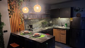 A modern kitchen with a central island, black cabinets, a stainless steel refrigerator, and hanging pendant lights. - Loft authentic coffee axis (Risaralda)