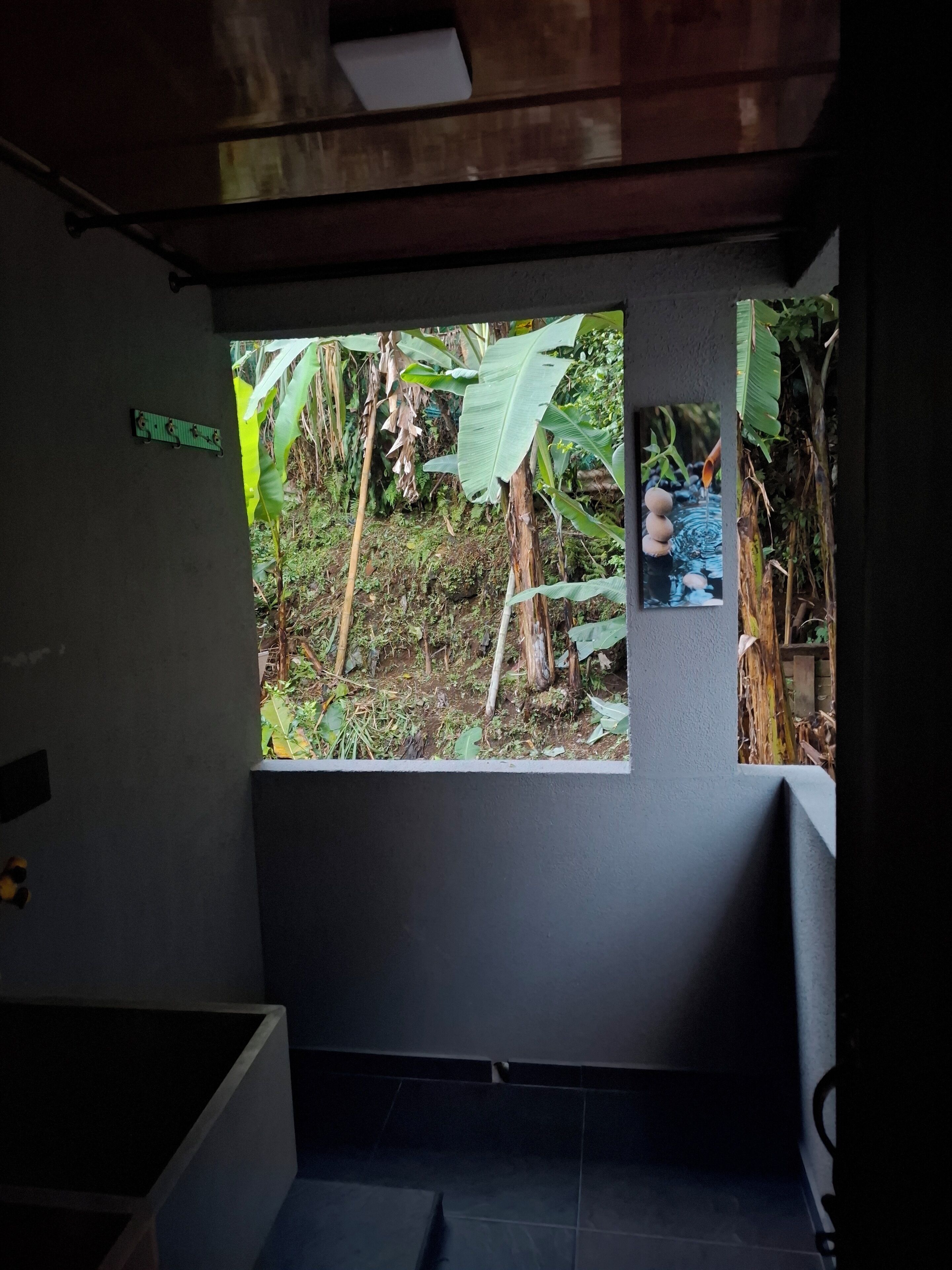 Ein Zimmer mit großem Fenster und Blick auf einen Garten mit Bananenpflanzen und einem Wasserspiel.