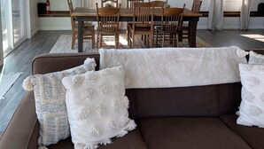 Una sala de estar moderna con un sofá marrón, almohadones blancos y un comedor con sillas de madera y una mesa.