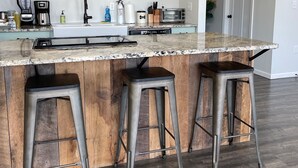 Una cocina con encimera de mármol, tres taburetes, una cafetera, un tostador y una licuadora.