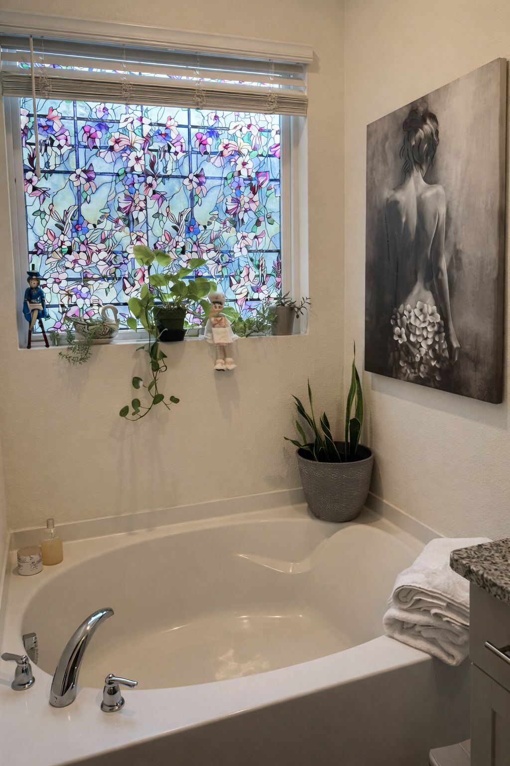 Ein Badezimmer mit einer Badewanne, einem Fenster mit floralem Buntglas und einem Bild an der Wand.