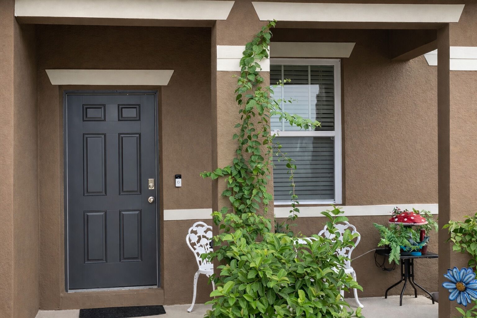 A front door, a white chair, a potted plant, and a small table with a potted plant.