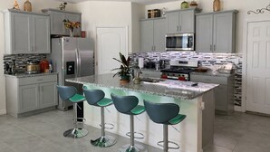 A modern kitchen with grey cabinets, a central island with bar stools, stainless steel appliances, and a tiled backsplash. - 2 BR Condo w/ Private Pool & Jacuzzi · Solterra Resort · 15 min to Disney Area (Davenport)