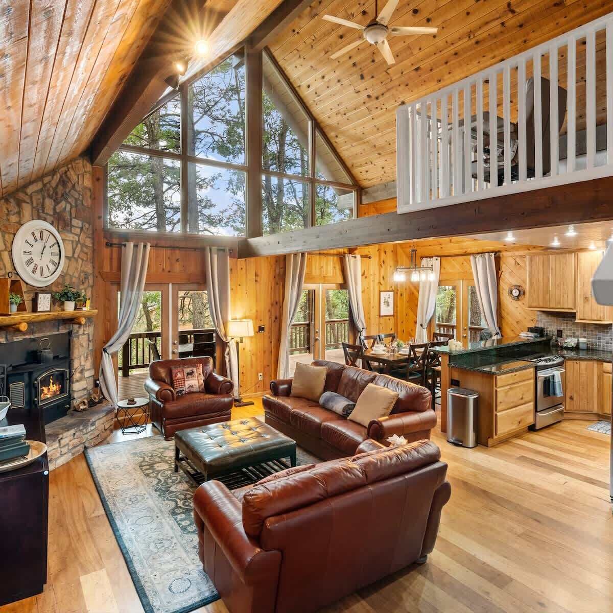A spacious living area with a fireplace, leather sofas, and a large window overlooking the outdoors.