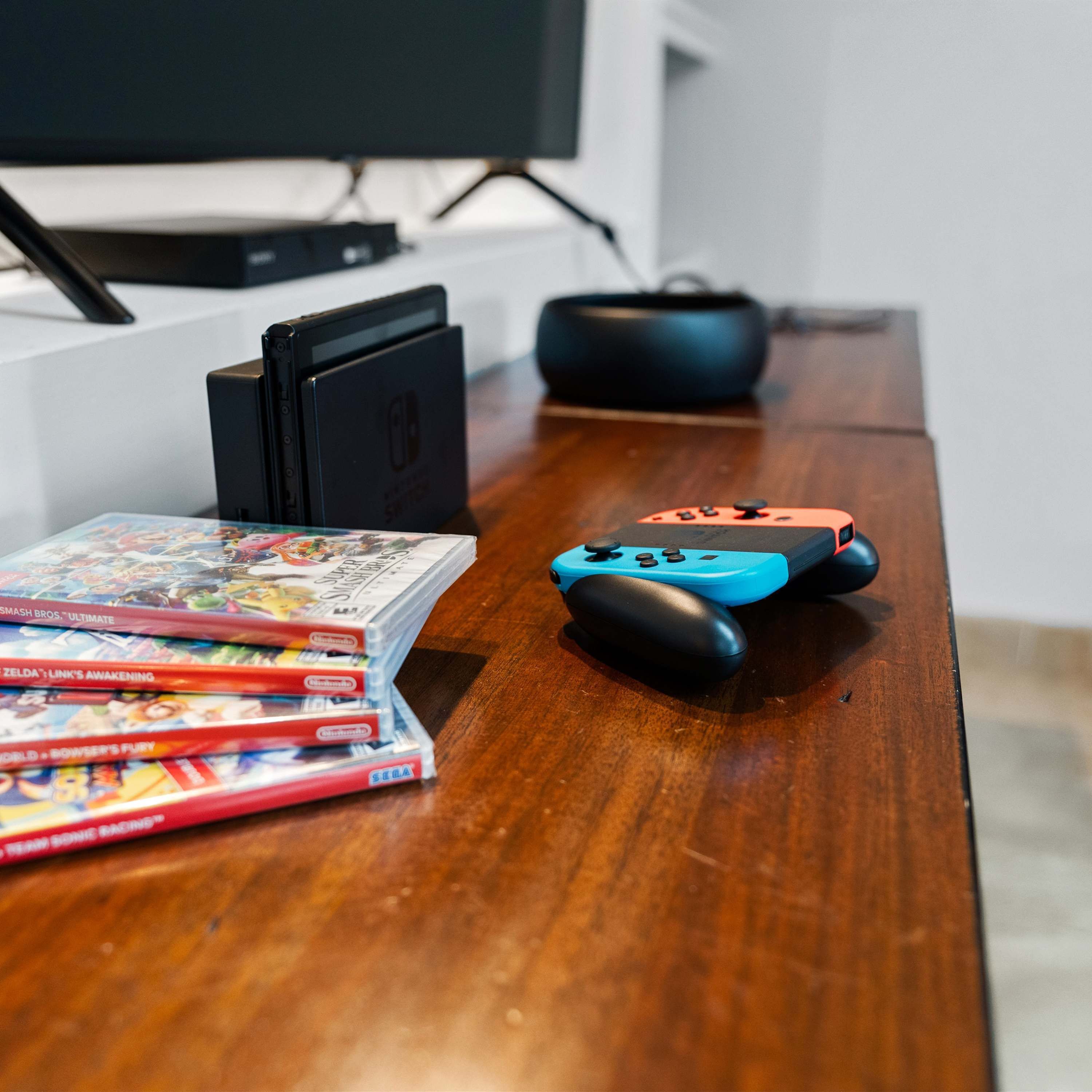 Une table en bois sur laquelle se trouvent une console Nintendo Switch, une manette de jeu bleue et orange, ainsi que plusieurs boîtiers de jeux vidéo.