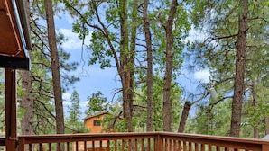 A deck with a fire pit, surrounded by trees and a distant cabin. - Family Cabin Retreat: Fireplace, Game Room, Outdoor Deck, Firepit (Munds Park)