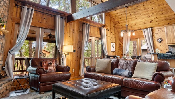 A spacious living room with leather sofas, a coffee table, and a large window offering a view of trees. - Family Cabin Retreat: Fireplace, Game Room, Outdoor Deck, Firepit (Munds Park)