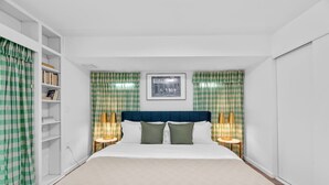 A neatly arranged bedroom with a bed, two bedside tables with lamps, a bookshelf, and checkered curtains. - Walk to OSU • 4BR Ranch • 3 Kings • Pet-Friendly (Columbus)