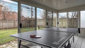 A ping pong table in a sunroom with large windows, a wooden fence, and a tiled floor. - Walk to OSU • 4BR Ranch • 3 Kings • Pet-Friendly (Columbus)