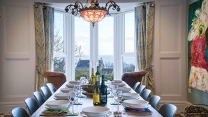 A dining room with a long wooden table set for a meal, large windows with curtains, and a view of the sea. - The Retreat - 5 Bedroom House - Horton (Swansea)