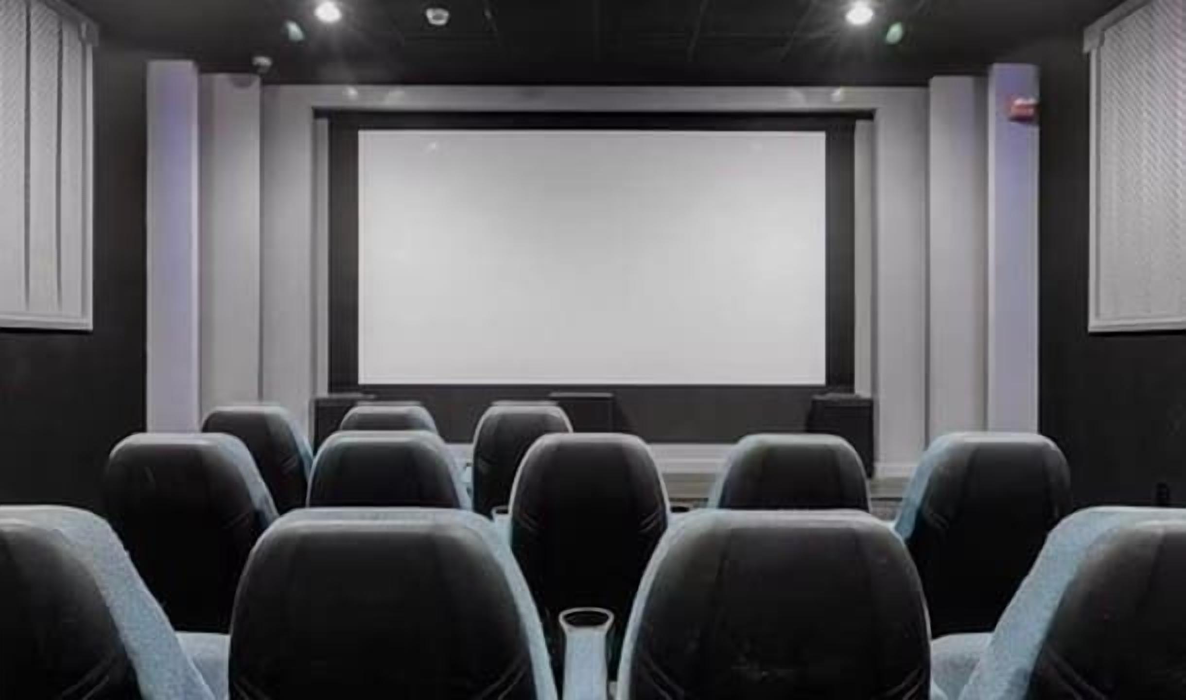 Une salle de conférence dotée d’un grand écran à l’avant, de rangées de chaises et d’un projecteur.