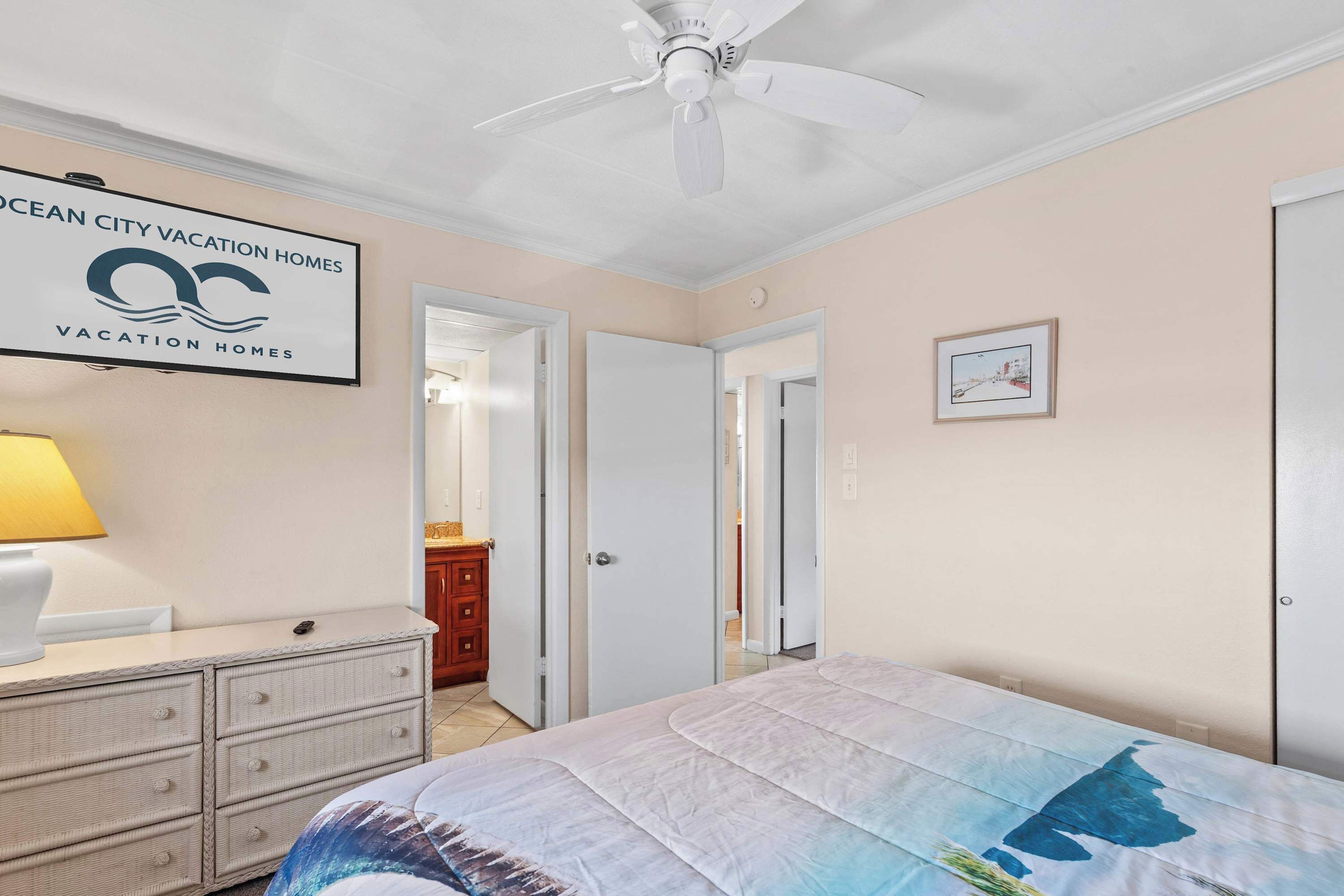 A bedroom with a bed, a dresser, a ceiling fan, and a sign for Ocean City Vacation Homes.