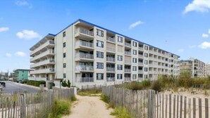 Un edificio residencial de varios pisos con balcones, un sendero de arena y una valla de madera.