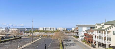 A parking lot with a row of buildings on the right, including a hotel with a balcony and a view of the ocean.