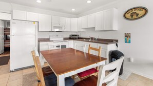 A compact kitchen with white cabinets, a wooden dining table, and a microwave. - Harbor Breeze #68 (Ocean City)
