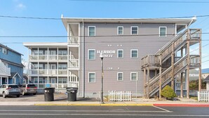 A multi-story building with a sign reading "Harbor Breeze." It features balconies, a stairway, and a parking area with cars. - Harbor Breeze #68 (Ocean City)