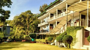 A multi-story building with balconies, a covered staircase, and a well-maintained lawn. - The Pine Oak Resort  (Bhimtal)