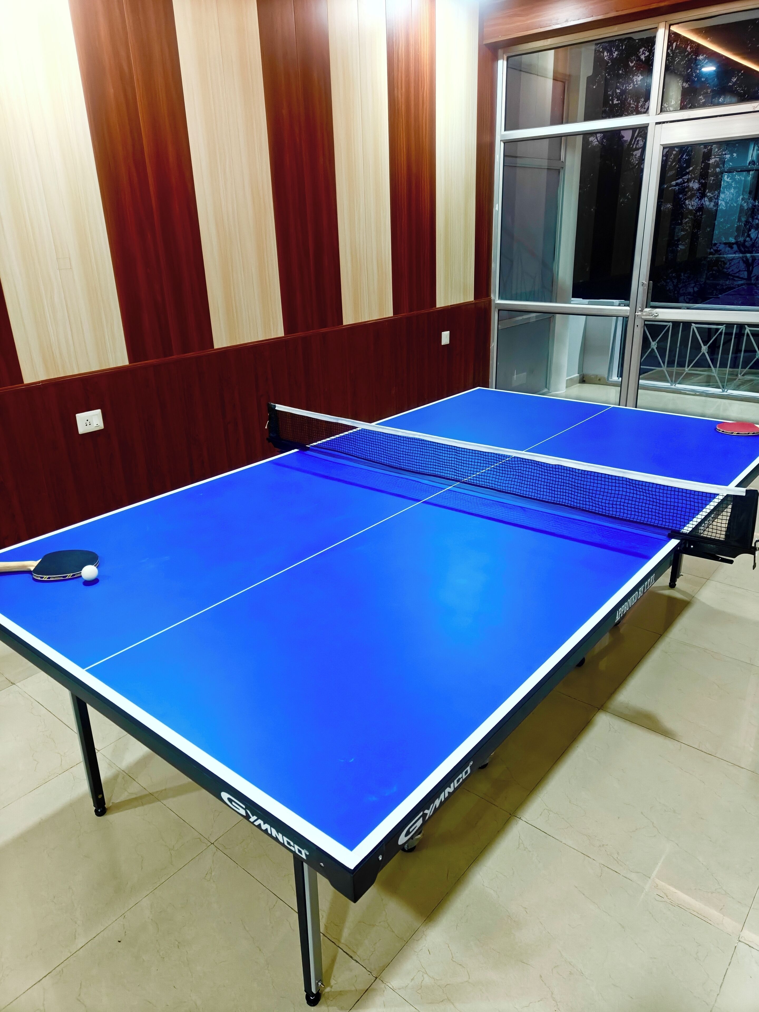 Una mesa de ping pong con red en una habitación con paneles de madera y una ventana.