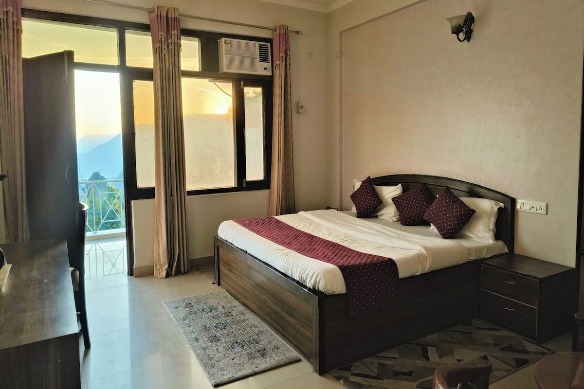 Quarto com cama, mesas de cabeceira, escrivaninha e vista para o exterior.