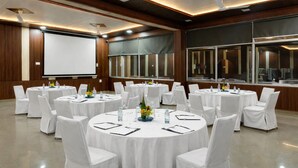 A conference room with multiple round tables, white chairs, and a projector screen. - The Pine Oak Resort  (Bhimtal)