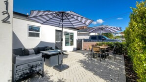 Eine Terrasse mit Gartenmöbeln, darunter eine Sitzecke und ein Tisch, sowie zwei große, gestreifte Sonnenschirme, die Schatten spenden.