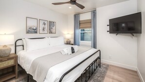 Ein modernes Schlafzimmer mit einem Bett, Nachttischen, einem Deckenventilator, einem Fernseher und Kunstwerken an der Wand.