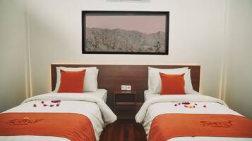 Ein Hotelzimmer mit zwei Betten, jeweils mit weißer Bettwäsche und orangefarbenen Akzenten, einem kleinen Nachttisch mit Steckdose und einem gerahmten Bild einer Berglandschaft an der Wand.