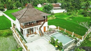 A two-story house with a balcony, a swimming pool, and lush green fields in the background. - Semu Villa (Pemenang)