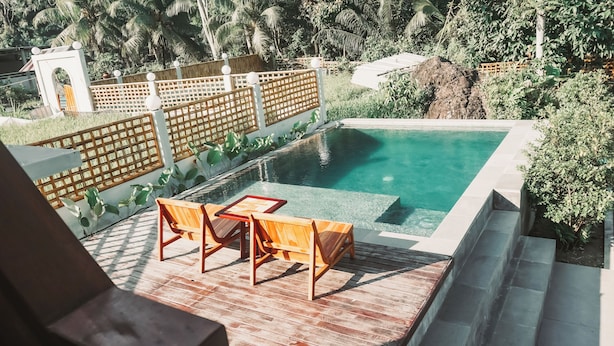 A rectangular swimming pool with clear water, surrounded by a wooden deck with two wooden chairs and a table. - Semu Villa (Pemenang)