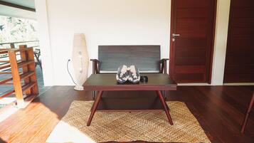 Una habitación con piso de madera, una mesa oscura con un tapete tejido, una silla, una lámpara alta de fibras naturales y una puerta de madera.