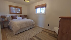 Ein Schlafzimmer mit Bett, Nachttischen, einem Fenster mit Jalousien, einer Deckenleuchte und einem Holzstuhl.