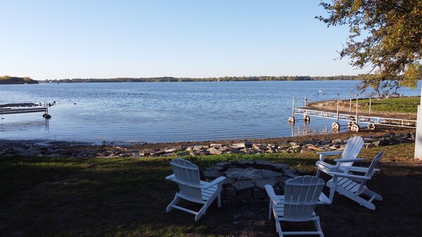 A lakeside view with a dock, a small pier, and three Adirondack chairs facing the water.