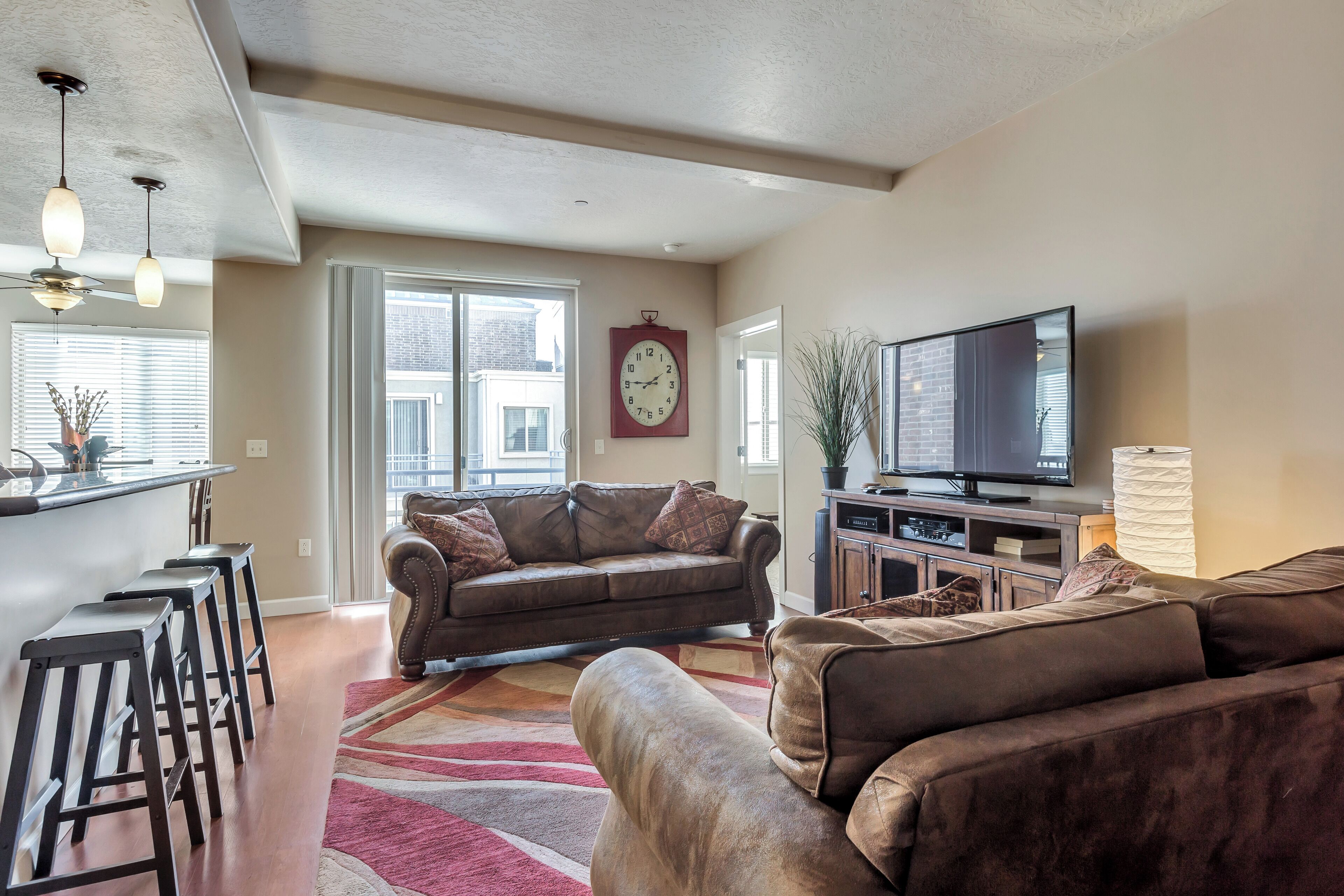 A spacious living room with a large brown leather sofa, a television, and a bar area with stools.