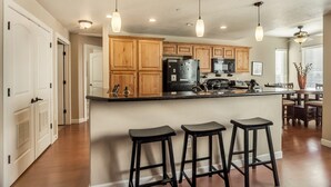A kitchen with wooden cabinets, a black refrigerator, a microwave, and a bar area with stools. - Condo Near Convention Center Sleeps 9 (Salt Lake City)