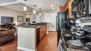 A modern kitchen with a central island, black appliances, wooden cabinets, and pendant lighting. - Condo Near Convention Center Sleeps 9 (Salt Lake City)
