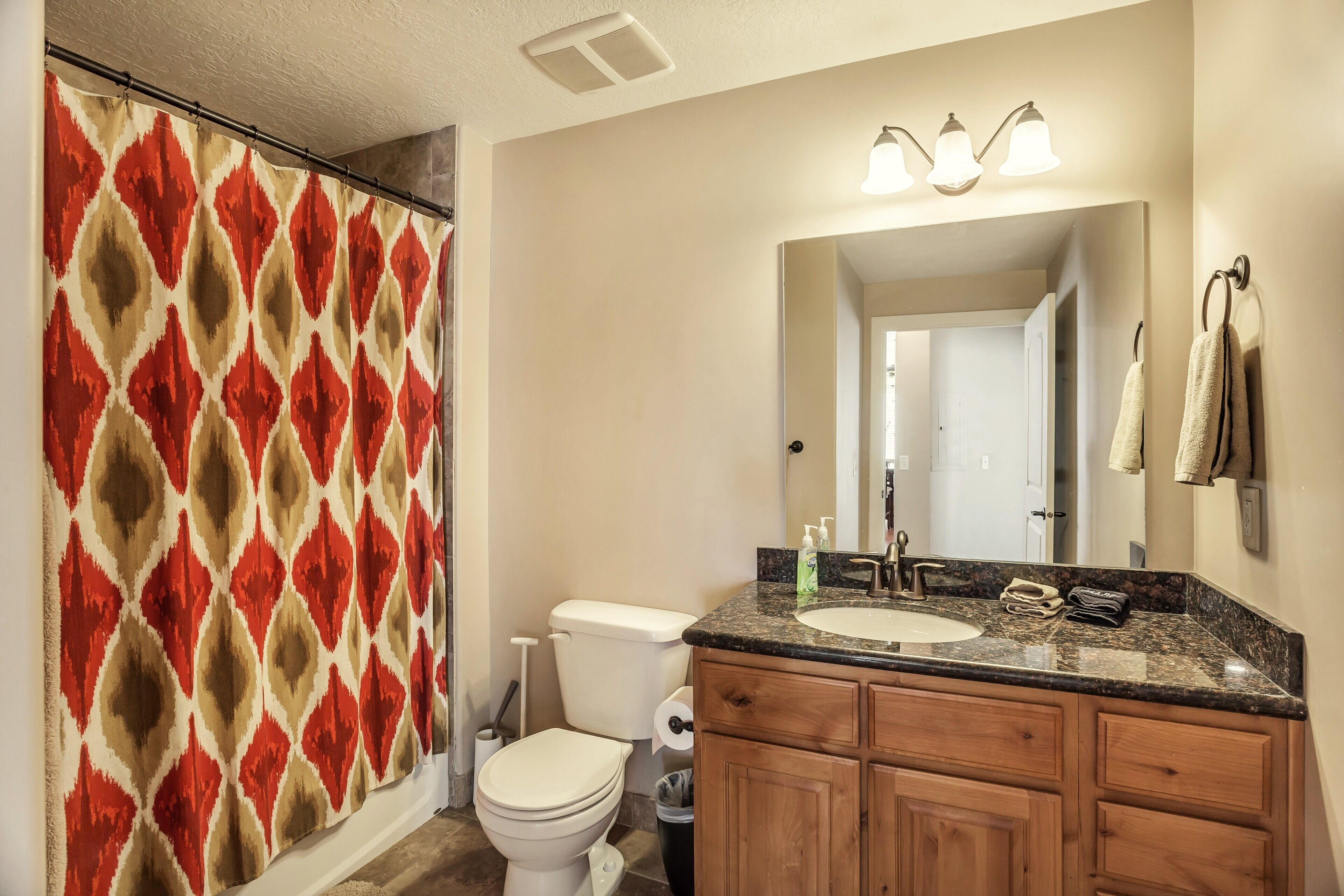 A bathroom with a shower curtain, toilet, sink, and wooden cabinets.