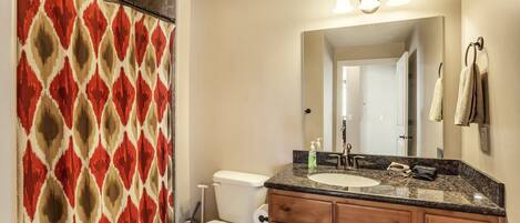 A bathroom with a shower curtain, toilet, sink, and wooden cabinets.