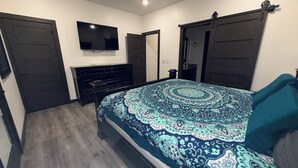 A bedroom with a bed, dresser, TV, and two doors. - “Haven” New 4 Bed 3.5 Bath w2 boat slips - Duchess Creek Estates - Porum Landing (PORUM)