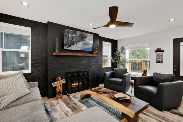 Ein modernes Wohnzimmer mit Kamin, zwei Ledersofas, einem Couchtisch und einem großen, an der Wand montierten Fernseher.