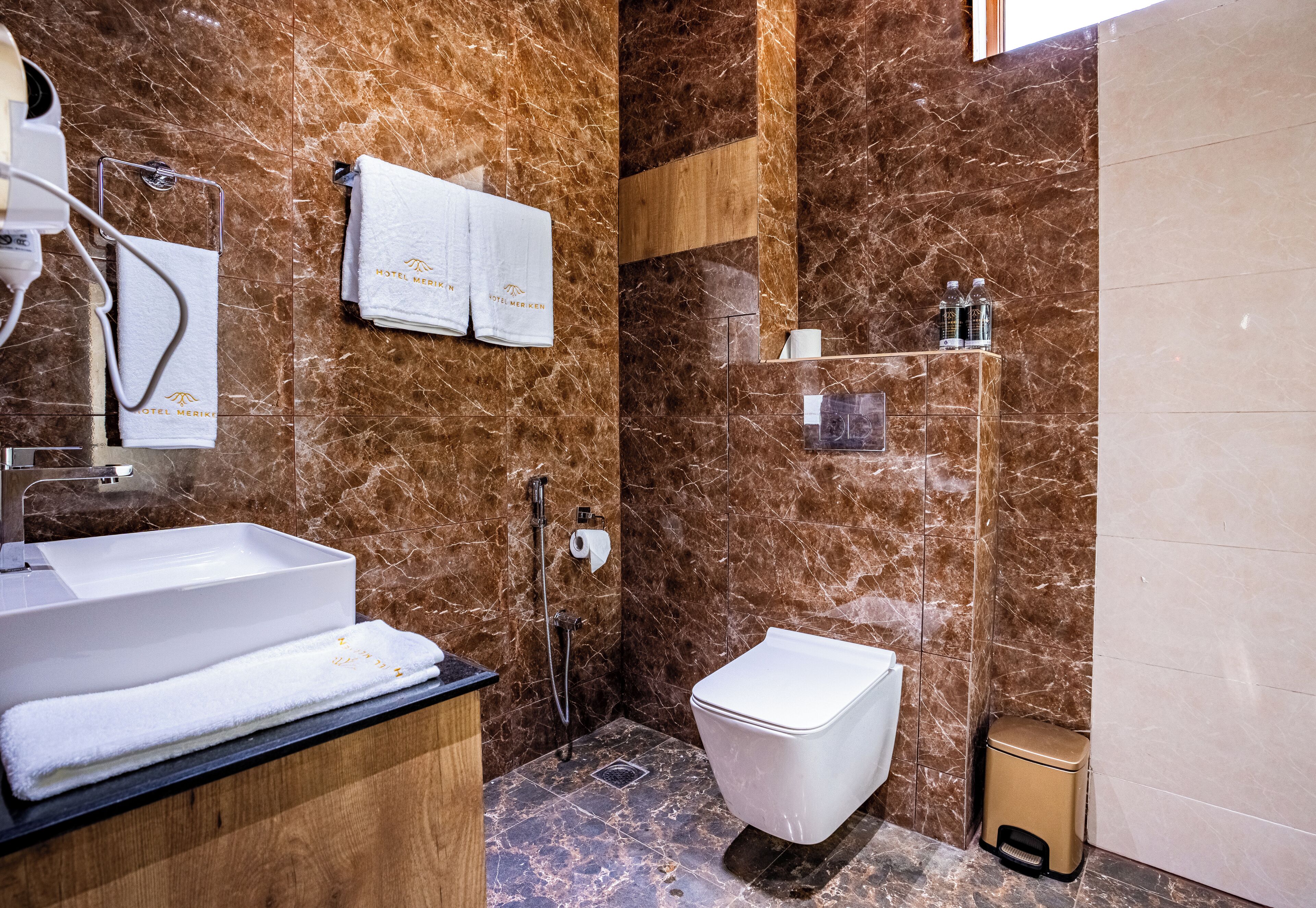 A bathroom with a marble wall, a sink, a toilet, and a shower area.