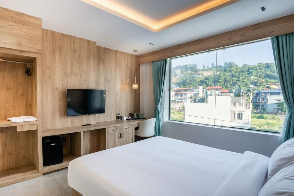 A modern hotel room with a wooden wall, a flat-screen TV, a desk with a chair, and a large bed.
