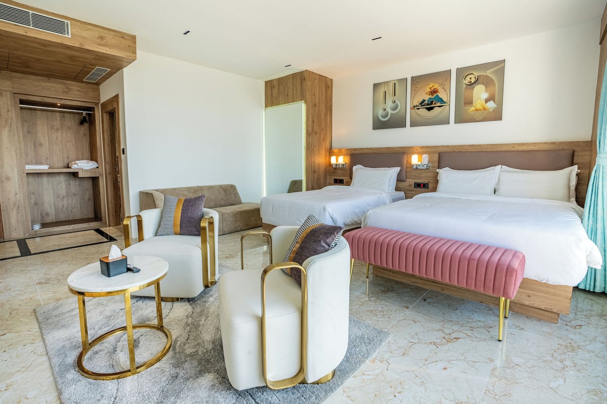 A modern hotel room with a large bed, two bedside tables, a sofa, and a small round table.